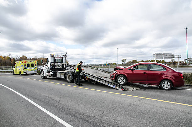 Quebec, Canada - October 18, 2015: Ambulance and tow truck towing an accidented car  on Du Marais street close to Capitale Highway in Quebec city during the day after an intervention following a car accident. We can see the tow man working.