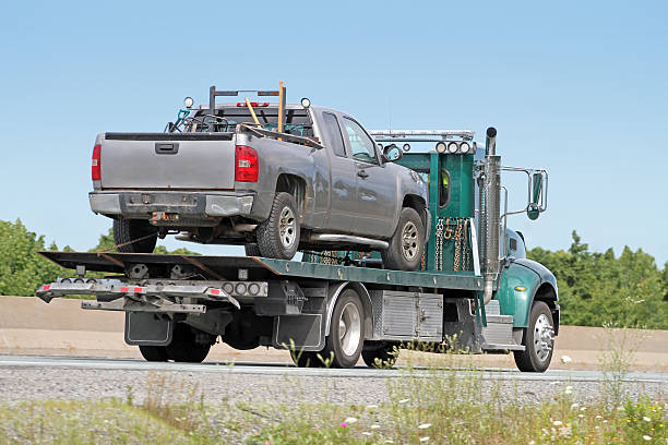 Rear quarter view of a tilt bed tow truck on a highway carrying an old model, unidentifiable,  nondescript half ton pick up truck.